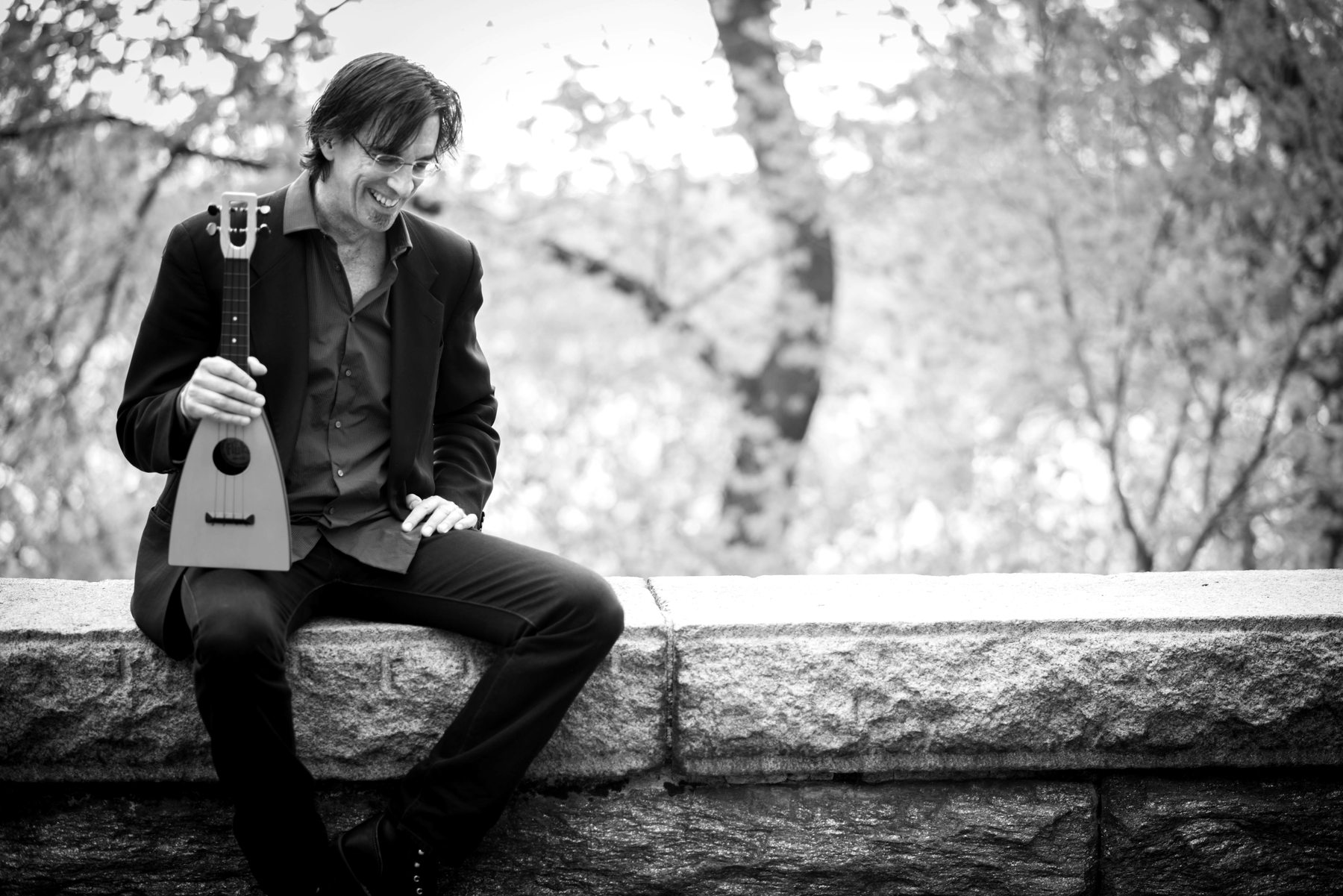 Ritt Henn laughing on a park wall with his ukulele